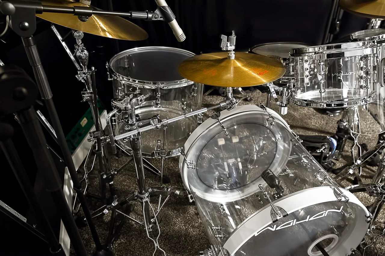 Das Acryl-Set schräg von vorn mit Becken, Toms und Bassdrum vor dunklem Vorhang